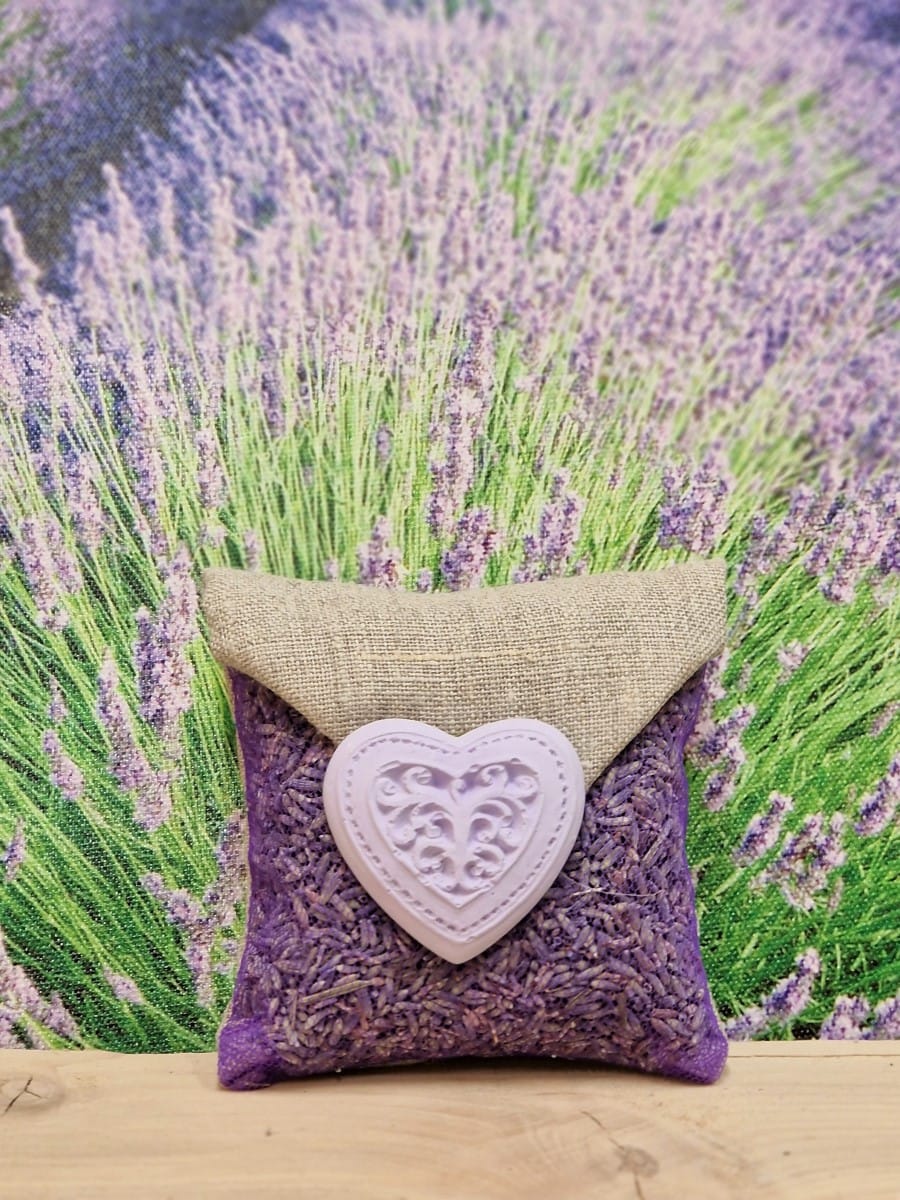 Sachet carré en lin et tulle violet garni de lavandin, orné d’un grand cœur volute en plâtre parfumable, à suspendre pour parfumer le linge.